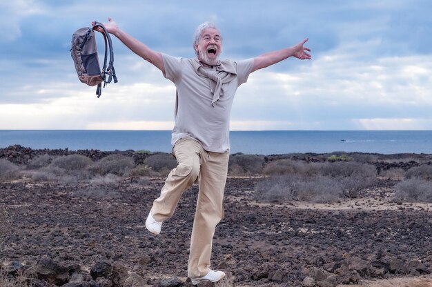 Abuelo emocionado loco saltando en una excursión al aire libre levantando una pierna con los brazos abiertos Hombre mayor