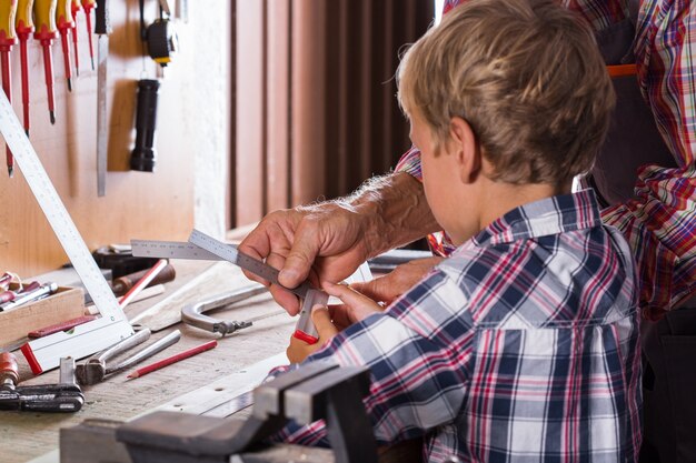 El abuelo enseña al niño a trabajar en un banco con herramientas de carpintería