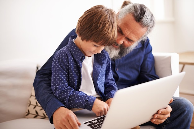 Abuelo hijo y computadora portátil en el sofá con amor y unión junto con juegos en línea en la sala de estar feliz niño de la familia y computadora para dibujos animados en el salón relajarse y suscripción a películas en vacaciones
