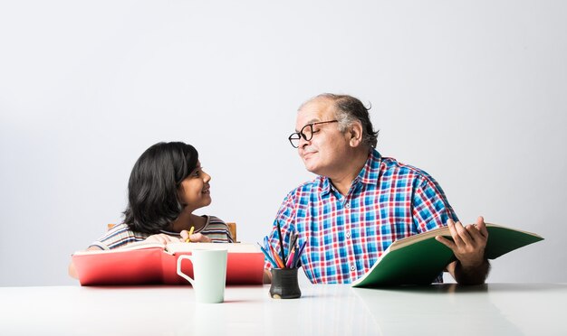 Abuelo indio enseñando a su nieta con libros, lápiz y computadora portátil, educación en el hogar o matrícula