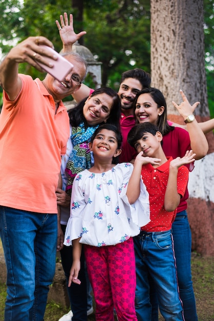 Abuelo indio tomando selfie - familia asiática de seis miembros de varias generaciones, capturando fotografías familiares en el teléfono inteligente mientras está de pie en el jardín o parque