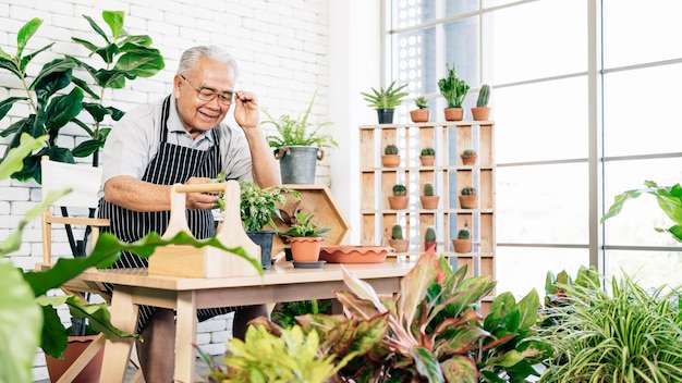 A un abuelo jubilado asiático le encanta cuidar las plantas en un jardín interior de la casa con una sonrisa y felicidad. Actividades de retiro.