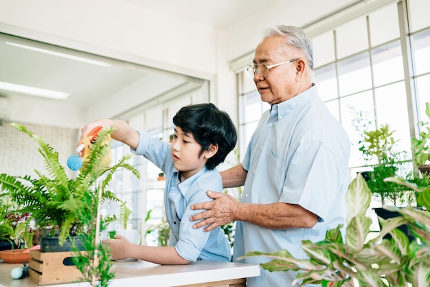 Un abuelo jubilado asiático y su nieto pasan tiempo de calidad juntos en casa. Disfruta de los cuidados regando las plantas. El vínculo familiar entre niños y adultos