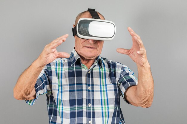 El abuelo mira los gestos con las manos de las gafas VR en un fondo gris