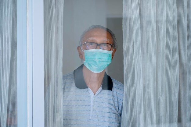 Abuelo mirando por la ventana con máscara