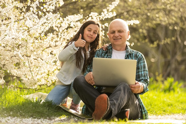 abuelo y nieta con laptop en el jardín.