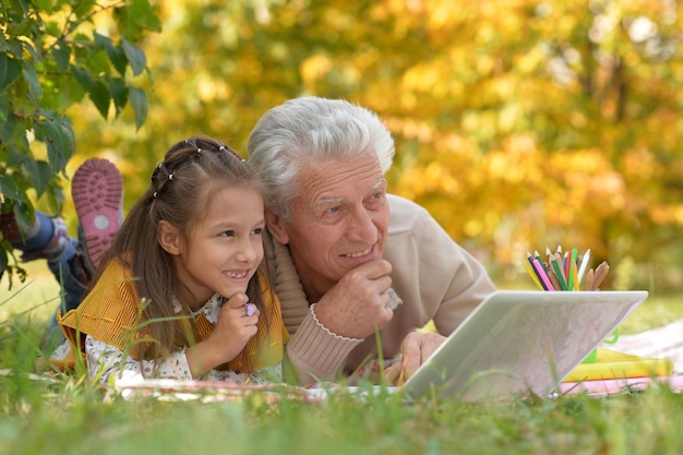 Abuelo y nieta leyendo un libro y usando una laptop al aire libre