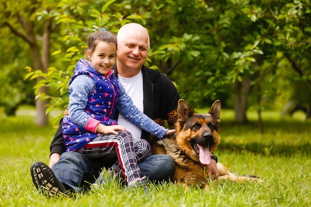 Abuelo con nieta y un perro en el jardín.