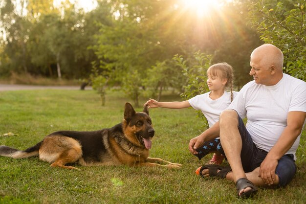 Abuelo con nieta y un perro en el jardín.