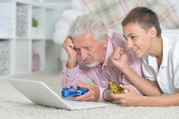 Abuelo y nieto acostado en el piso y jugando juegos de computadora en la computadora portátil