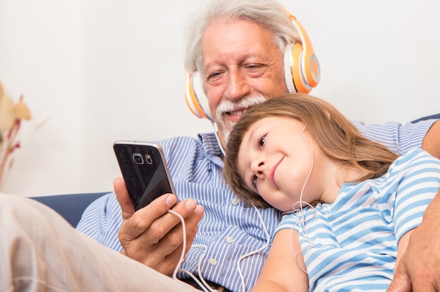 Abuelo y nieto con auriculares escuchan música abrazándose en el sofá