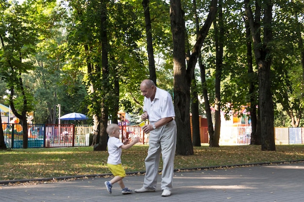 Abuelo y nieto están caminando en el parque a lo largo del camino con un vaso de palomitas de maíz Un anciano y un niño pequeño tienen bocadillos para llevar