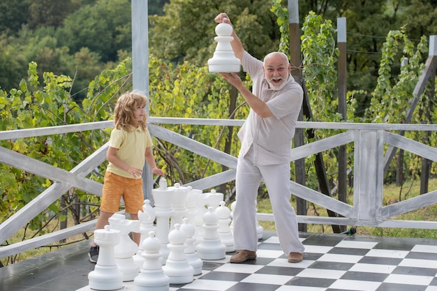 Abuelo y nieto jugando al ajedrez en un gran tablero de ajedrez anciano pariente ingenio niño