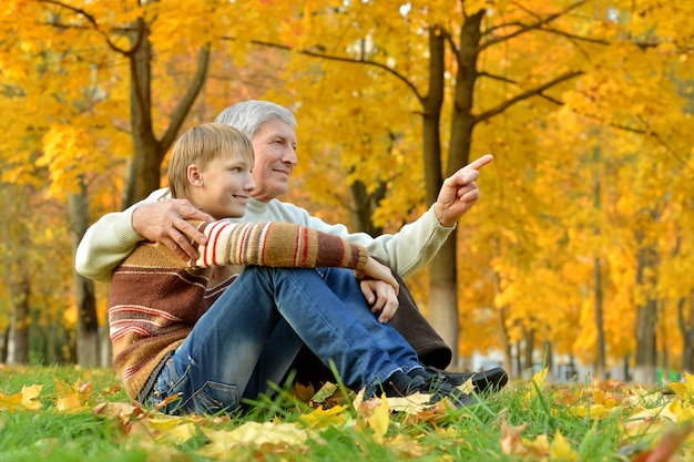 Abuelo con niño descansando en el parque de otoño, niño cierra los ojos del abuelo