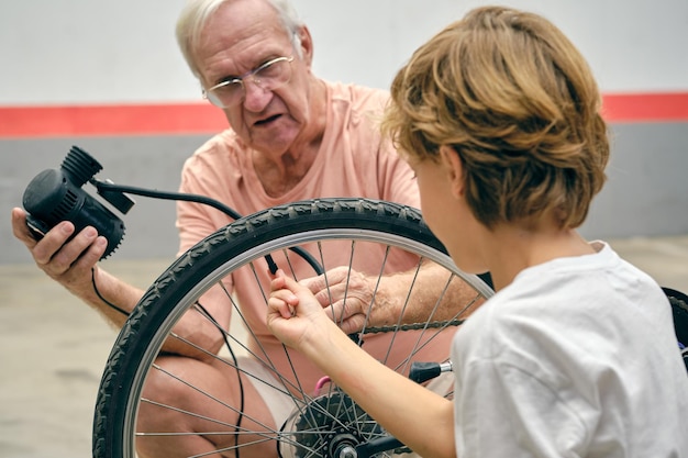 Abuelo y niño pequeño con bomba pasando tiempo juntos mientras inflan neumáticos de bicicleta