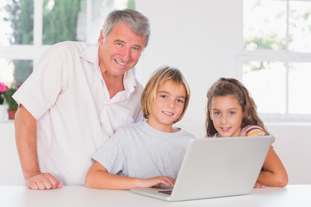 Abuelo y niños mirando a la cámara con la computadora portátil en frente