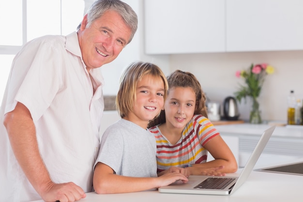 Abuelo y niños mirando a la cámara junto con la computadora portátil en frente