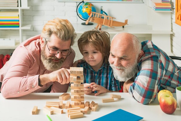 Abuelo padre e hijo alumno sonriendo contra el fondo del hogar Feliz generacional muti tres generaciones hombres retrato familiar Jenga juego en casa