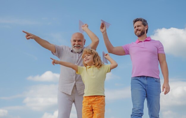 Abuelo padre e hijo jugando con avión de papel al aire libre en el cielo familia feliz tres hombres generatio