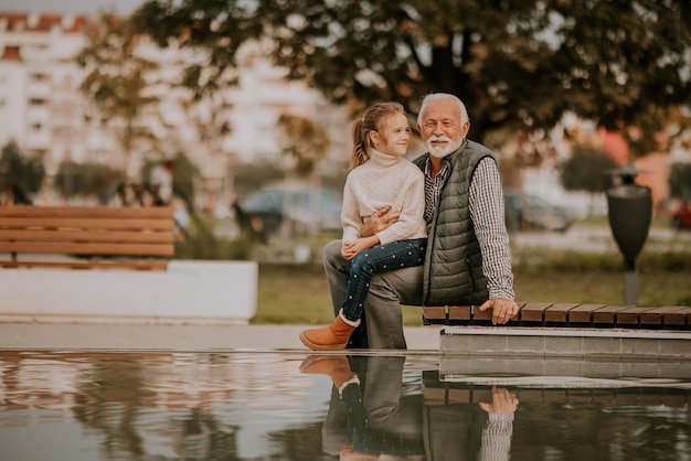 El abuelo pasa tiempo con su nieta junto a una pequeña piscina de agua en el parque el día de otoño