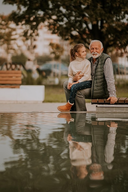 El abuelo pasa tiempo con su nieta junto a una pequeña piscina de agua en el parque el día de otoño