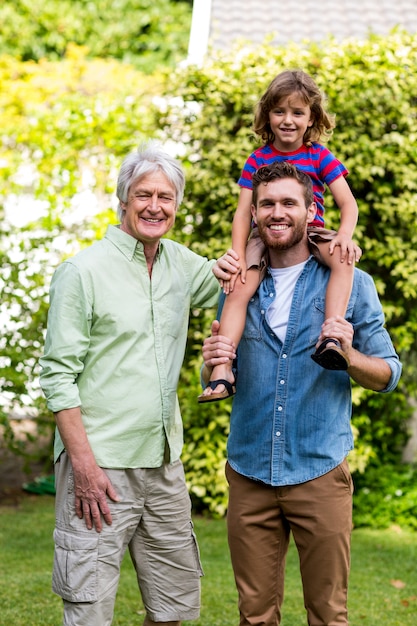 Abuelo de pie con hijo llevando nieto en el patio