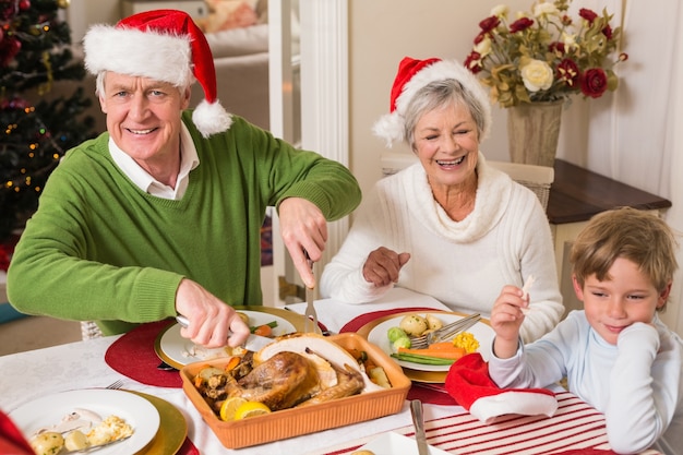 Abuelo en el sombrero de santa que talla el pavo asado en la Navidad