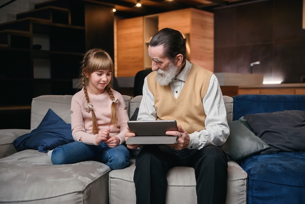 Abuelo con su nieta usando tableta en casa acogedora.