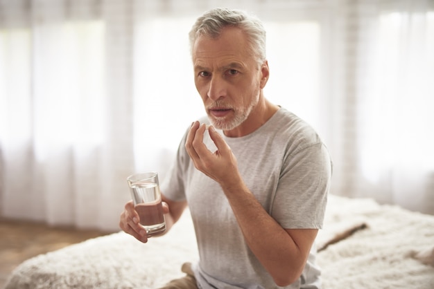 Abuelo tomando pastillas en el dolor crónico matutino.