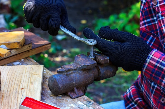 El abuelo trabaja en un taller forestal el abuelo aprieta una tuerca en un perno que está sujeto en un tornillo de banco