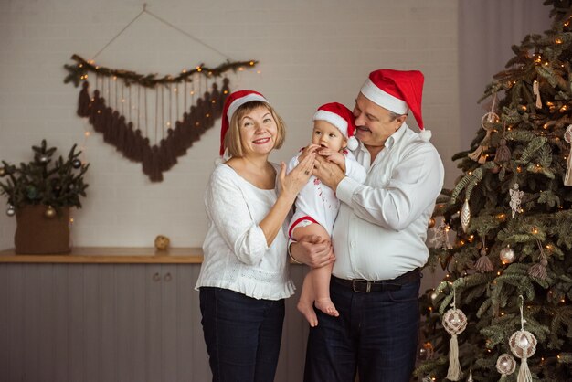 Abuelos felices y nieto con sombreros de Santa cerca del árbol de Navidad