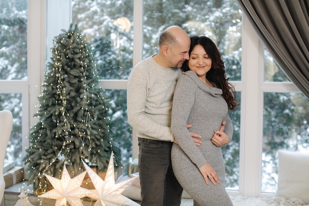 Abuelos felices parados frente a abeto y esperando la Navidad