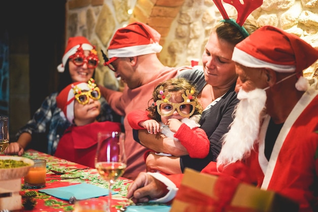 Abuelos, hijos, madre, padre y hermana abriendo regalos de Navidad con gafas divertidas y gorros de santa