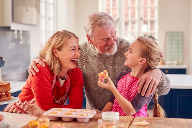 Abuelos con nieta comiendo pastelitos caseros en la cocina en casa