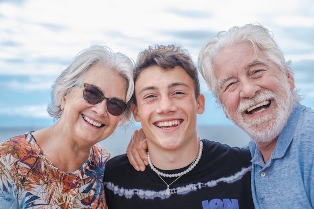 Abuelos con nieto adolescente abrazándose en el mar divirtiéndose juntos sonriendo