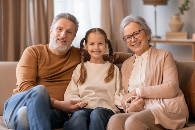 Abuelos sonrientes sentados con su nieta en un sofá beige