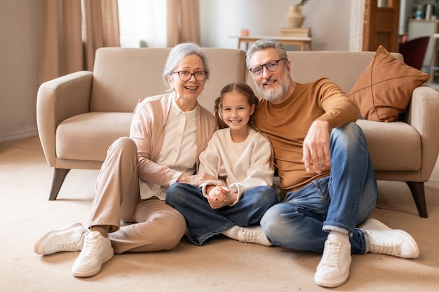 Los abuelos sonrientes sentados en el suelo de la sala de estar con la nieta joven