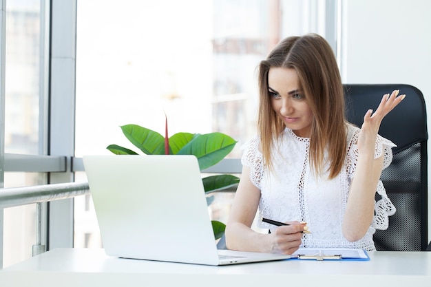 Aburrida mujer joven en la oficina trabajando con una computadora portátil y mirando a la pantalla de la computadora