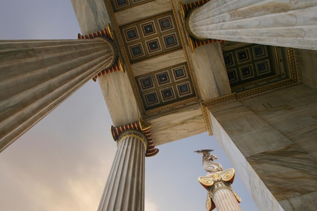 Foto academia de atenas uma coluna de mármore com esculturas de atenas contra uma com nuvens em atenas grécia