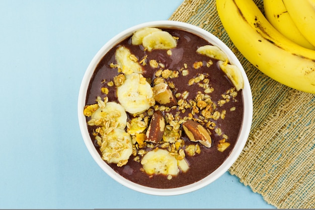 Açaí brasileiro em uma tigela branca com banana, granola e castanhas.