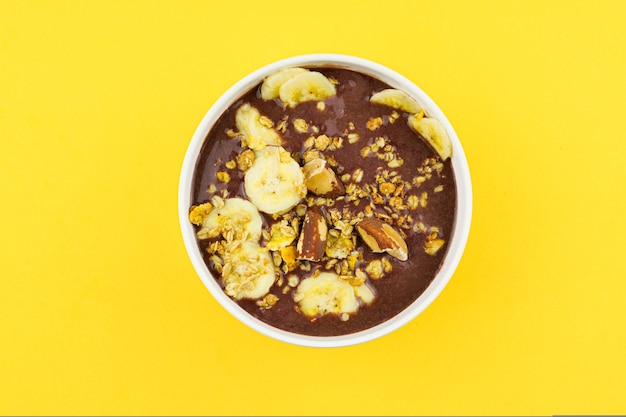 Açaí brasileiro em uma tigela branca com banana, granola e castanhas.