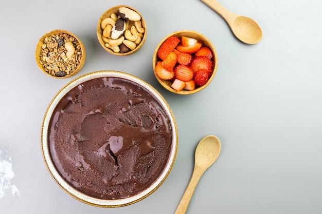 Acai brasileño en un tazón blanco granola de fresa adicional y nueces en pequeños tazones de bambú Anacardos y Para Vista superior Fondo gris Enfoque selectivo