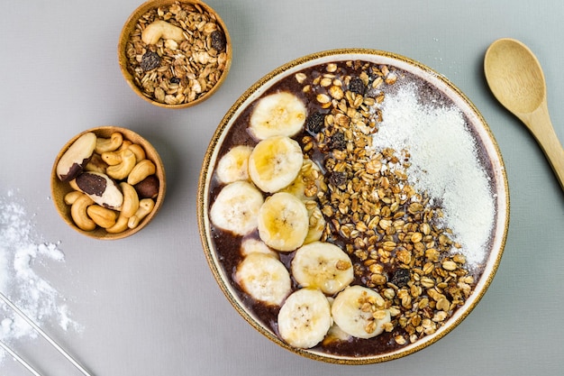 Acai brasileño en un tazón blanco con granola de miel de leche en polvo de plátano y nueces en pequeños tazones de bambú Anacardos y Para Vista superior Fondo gris Enfoque selectivo