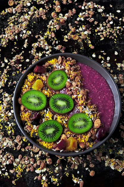 Acai Schüssel mit Müsli und Kiwi auf dem Hintergrund von verstreutem Müsli.