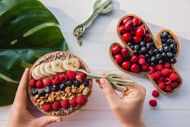 Açaí smoothie granola sementes frutas frescas em uma tigela de madeira na mão feminina