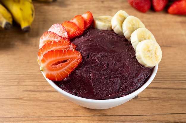 Açai, tazón de helado brasileño congelado de bayas de Acai con fresas y plátanos. con frutas en mesa de madera. Vista frontal del menú de verano