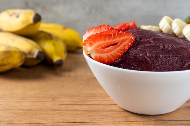 Açai, tazón de helado brasileño congelado de bayas de Acai con fresas y plátanos. con frutas en mesa de madera. Vista frontal del menú de verano