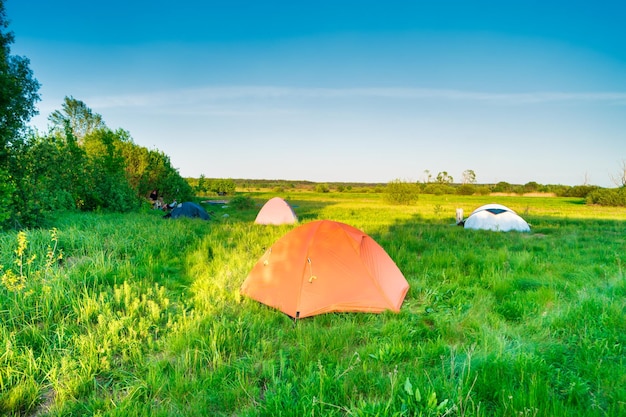 Acampamento de barraca ao pôr do sol no campo de grama verde na floresta