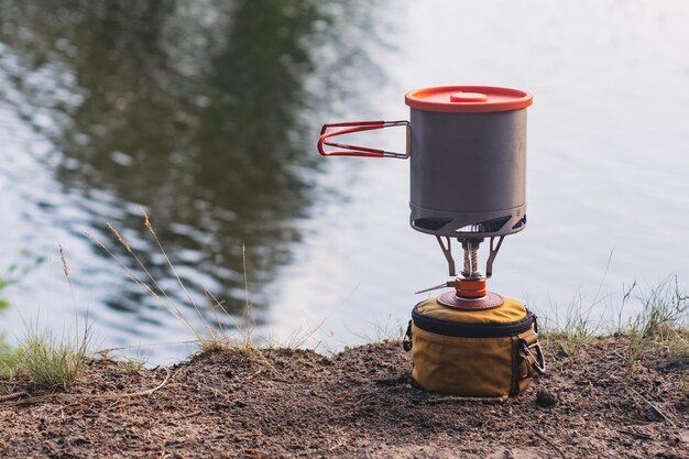 Acampamento de verão ao ar livre contra o fundo do lago Queimador de gás turístico com panelas para cozinhar