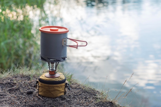 Acampamento de verão ao ar livre contra o fundo do lago Queimador de gás turístico com panelas para cozinhar